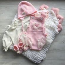 Pink knit romper, hat booties, blouse and white blanket with four pink hearts.
