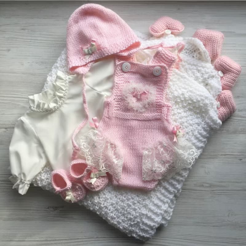 Pink knit romper, hat booties, blouse and white blanket with four pink hearts.