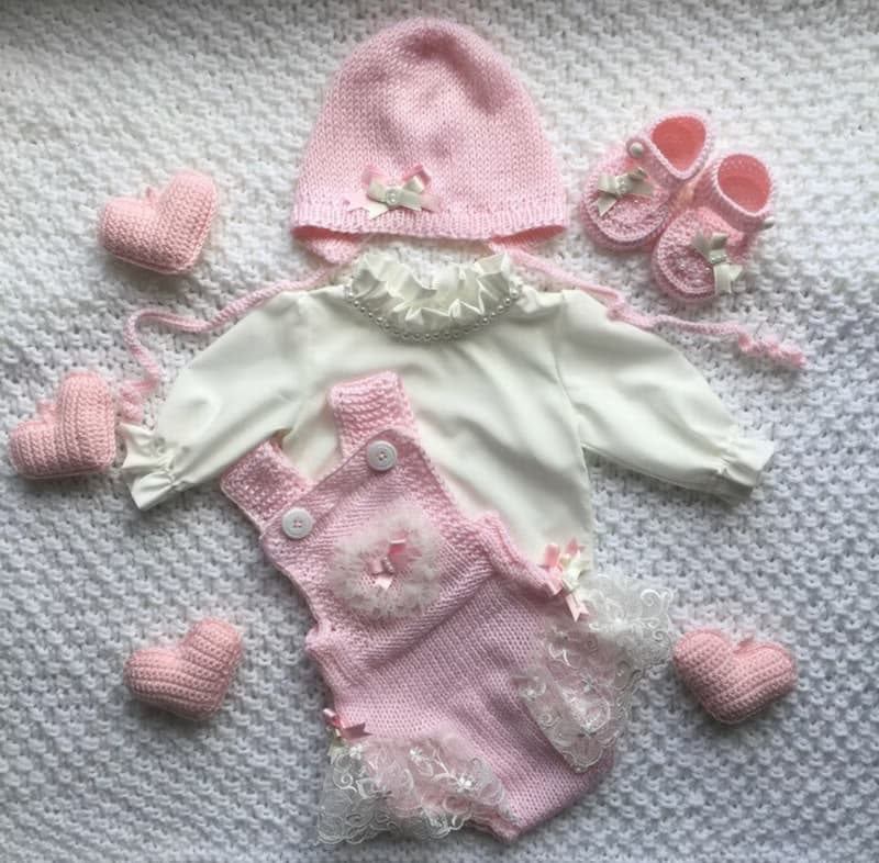 Pink knit romper, hat booties, blouse and white blanket with four pink hearts.