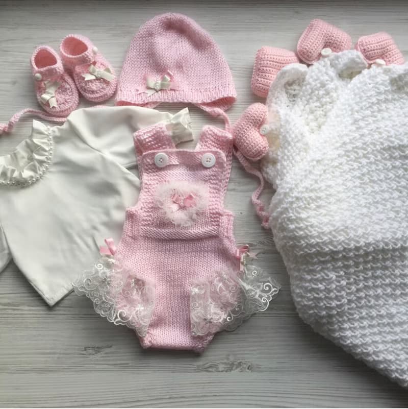 Pink knit romper, hat booties, blouse and white blanket with four pink hearts.