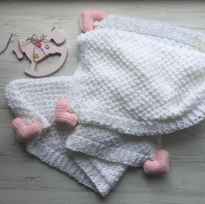 Pink knit romper, hat booties, blouse and white blanket with four pink hearts.