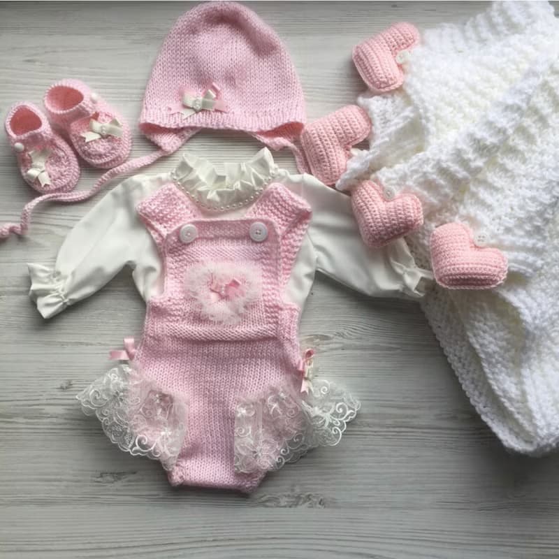 Pink knit romper, hat booties, blouse and white blanket with four pink hearts.