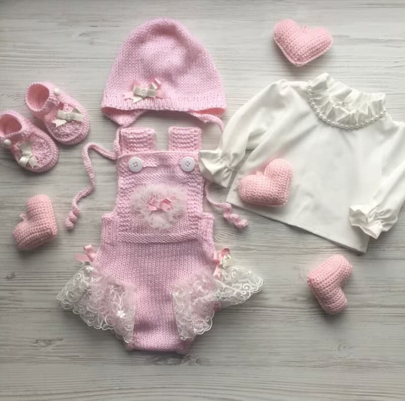 Pink knit romper, hat booties, blouse and white blanket with four pink hearts.