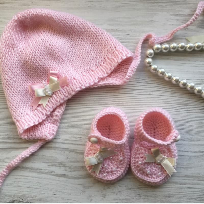Pink knit romper, hat booties, blouse and white blanket with four pink hearts.